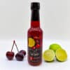 Flasche Kirsch Limetten Sirup mit frischen Kirschen und halbierten Limetten vor weißem Hintergrund