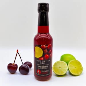 Flasche Kirsch Limetten Sirup mit frischen Kirschen und halbierten Limetten vor weißem Hintergrund